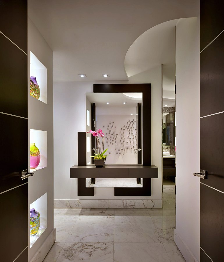 Entry with a dark-framed mirror, floating console and lit niches